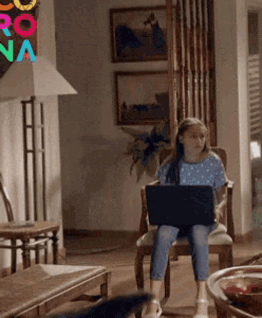 a little girl is sitting in a chair with a laptop in front of a sign that says rona