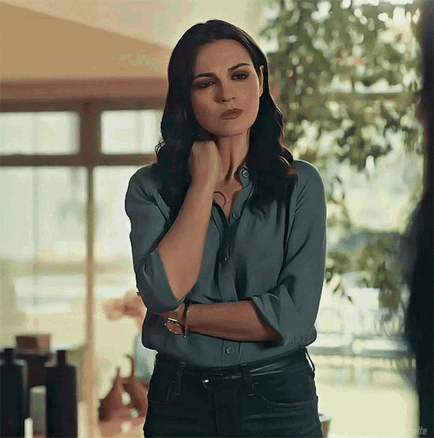a woman in a blue shirt and black jeans is standing with her arms crossed