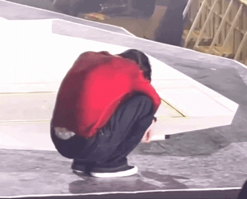 a man in a red shirt and black pants is squatting down