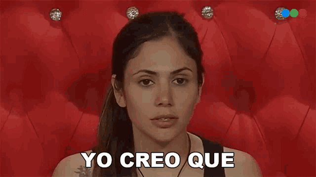 a woman is sitting in front of a red couch and saying yo creo que .