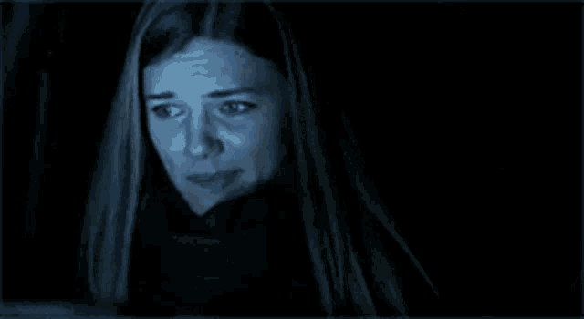 a woman with long hair and blue eyes is looking at the camera in the dark .