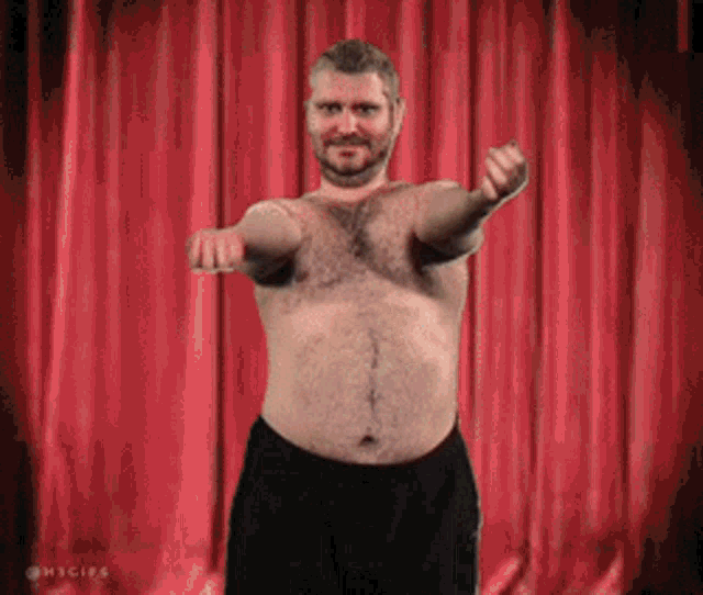 a shirtless man is standing in front of a red curtain with his arms outstretched