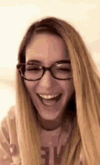 a young woman wearing glasses is laughing and making a funny face .