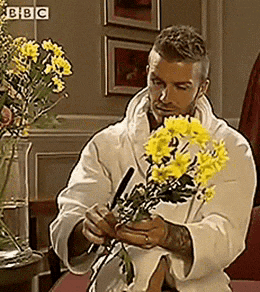a man in a white robe is holding a bouquet of yellow flowers in front of a bbc sign