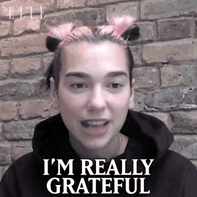 a woman with pink hair says i 'm really grateful in front of a brick wall