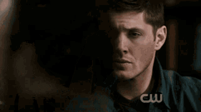 a man holds his hand to his forehead in front of a cw logo