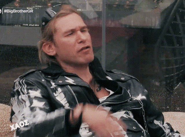 a man wearing a black and white jacket is sitting on a couch in front of a big brother logo