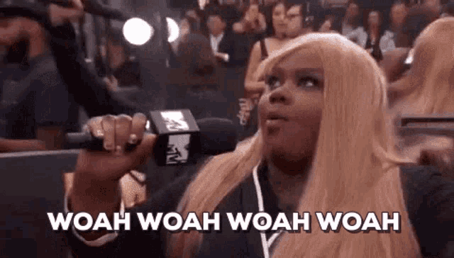 a woman is holding a microphone and saying woah woah woah woah in front of a crowd .