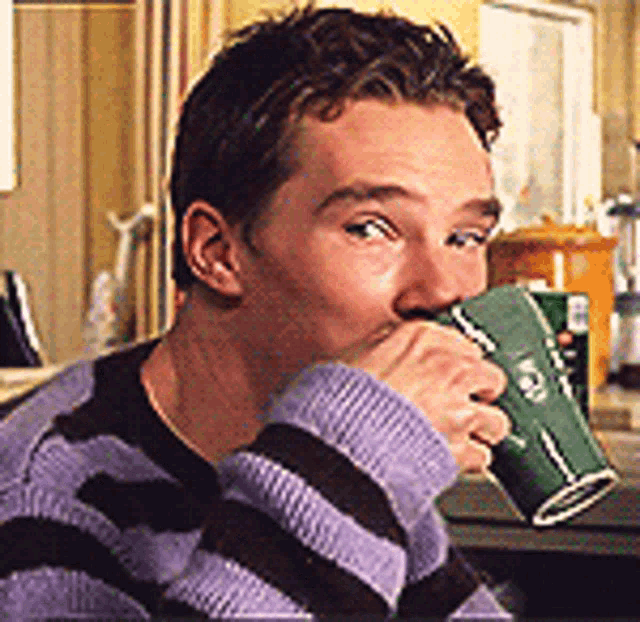 a man in a striped sweater drinking from a green cup