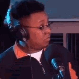 a man wearing headphones and glasses is talking into a microphone in a studio .