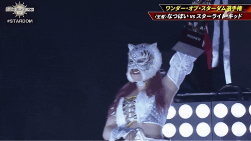 a woman in a tiger mask is holding a trophy in front of a sign that says #stardom