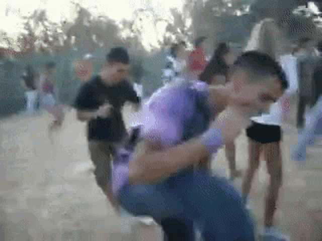 a man in a purple shirt is carrying another man in a crowd .