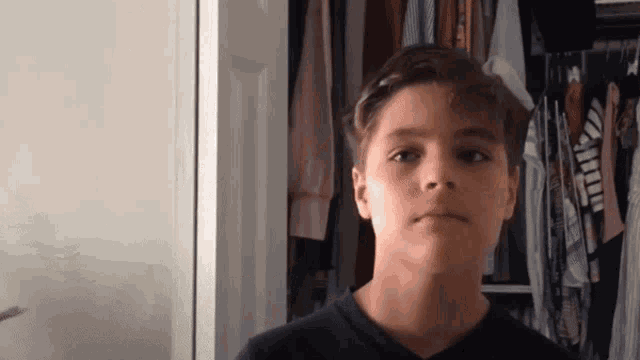 a young boy standing in front of a closet full of clothes