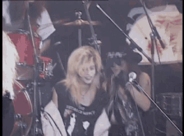 a woman is singing into a microphone on a stage while a man plays drums .