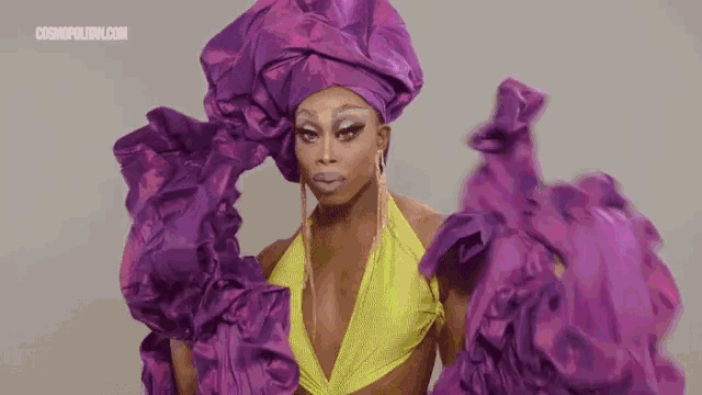 a drag queen is wearing a purple and yellow dress and a purple headpiece .