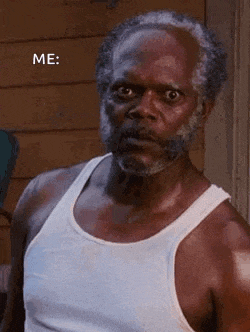 a man with a beard is wearing a white tank top and looking at the camera .