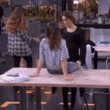 a woman sits on a wooden table while two other women stand around her