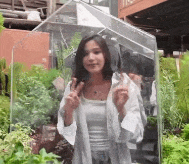 a woman is standing in front of a greenhouse with plants behind her .