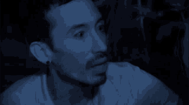 a man with a beard and ear plugs looks surprised in the dark