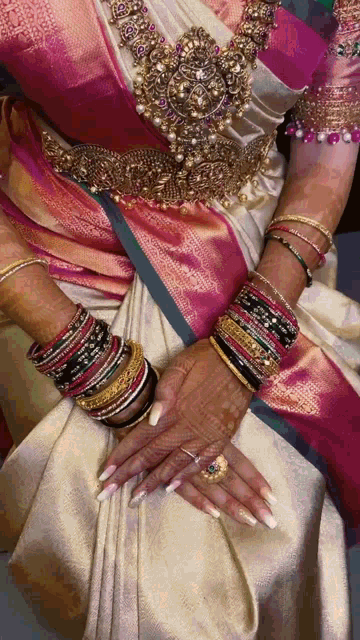 a woman wearing a pink and white saree and a lot of bracelets on her wrists
