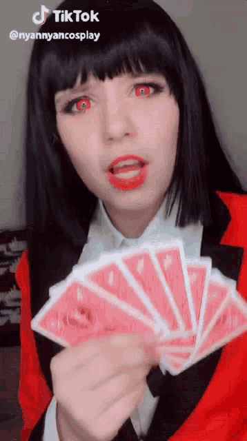 a woman in a red jacket is holding a fan of red playing cards