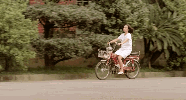 a woman in a white dress is riding a red motorcycle with a basket on the front