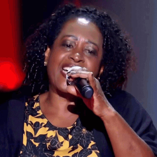 a woman singing into a microphone with a yellow and black dress on
