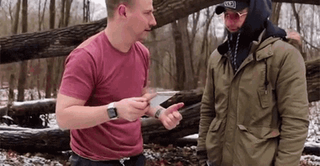 two men are standing next to each other in the woods .
