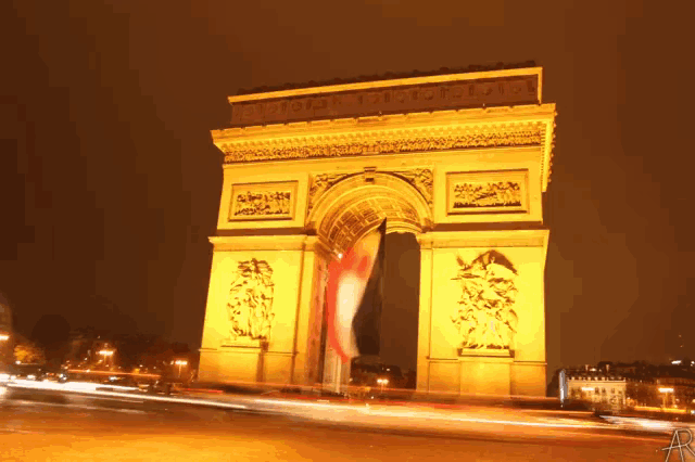 the triumphal arch is lit up at night and has a flag hanging from it