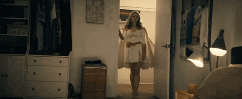 a woman in a white dress is standing in a room with a clock on the wall that says 9:12