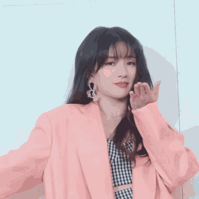 a woman wearing a pink jacket and earrings is waving