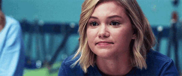 a woman in a blue shirt is making a funny face while sitting at a table in a classroom .