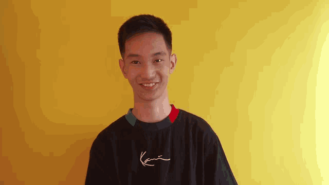 a young man wearing a black karl kani t-shirt smiles for the camera
