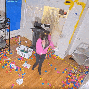 a woman in a pink shirt is standing in a room filled with balls