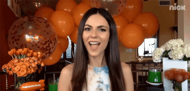 a woman is standing in front of a bunch of orange balloons with a nick logo on the bottom right