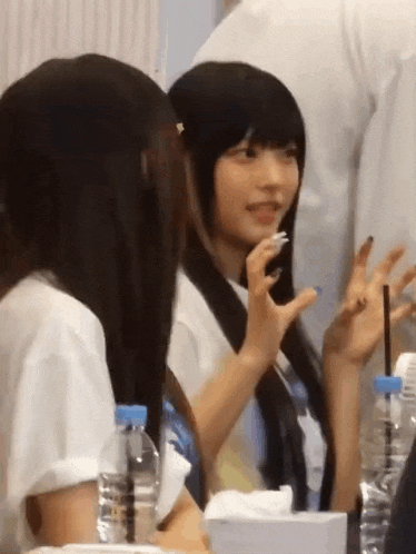 two girls are sitting at a table with bottles of water .