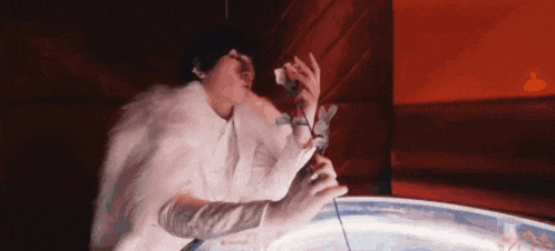 a woman in a white fur coat is singing into a microphone while holding a flower .