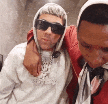 a man wearing sunglasses and a hoodie with the word ice on it is standing next to another man wearing sunglasses