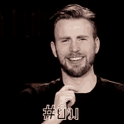 a man with a beard is smiling and holding his hand to his chin .