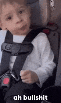 a little boy is sitting in a car seat and making a face .