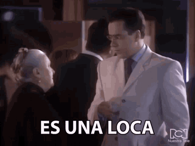 a man in a white suit stands next to an older woman with the words es una loca below him