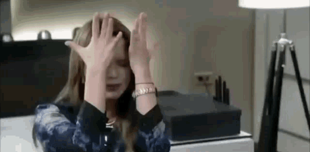 a woman is covering her face with her hands while sitting at a desk .