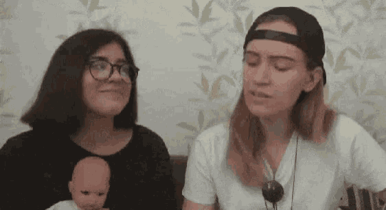 two women are sitting next to each other holding a baby doll .