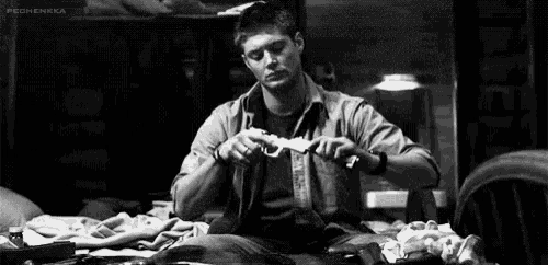 a black and white photo of a man sitting at a table cutting a piece of paper .