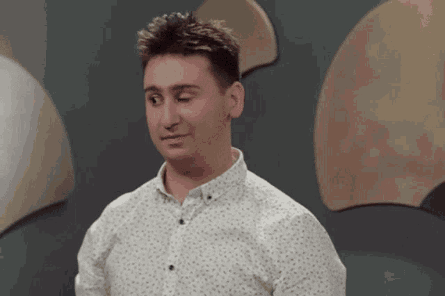 a man in a white shirt is standing in front of a wall with circles on it .