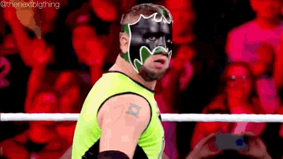 a wrestler wearing a green and black mask is standing in a ring