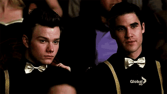 two men wearing bow ties and suspenders are sitting in a crowd on global hd