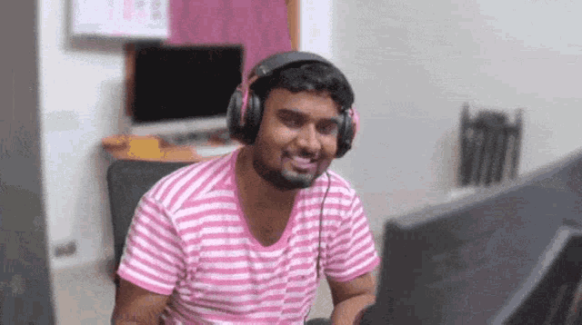 a man wearing headphones is smiling while looking at a computer monitor