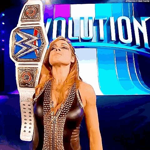 a woman in a black dress is holding a wrestling championship belt in front of a sign that says evolution .
