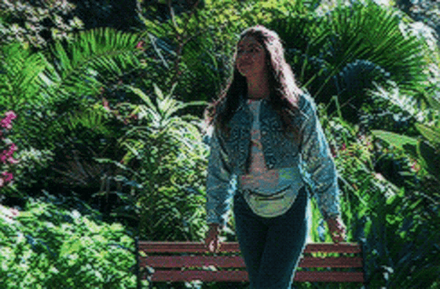 a woman in a denim jacket is walking across a park bench